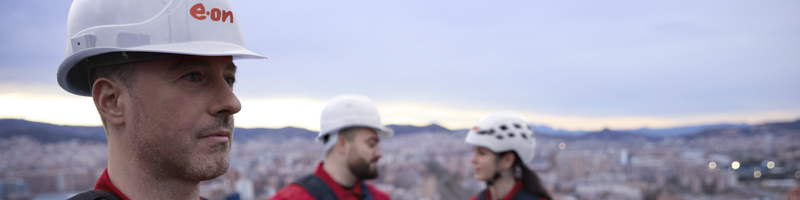A worker in an E.ON branded hard hat, with two other workers seen chatting in the background