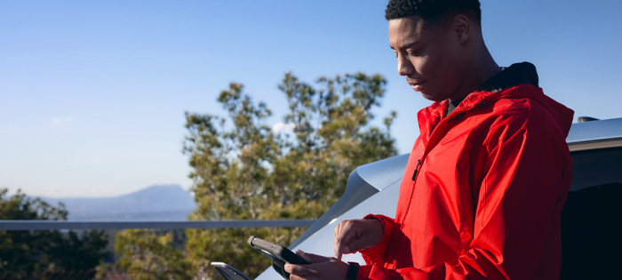 A person leaning against a car looks down at a mobile device