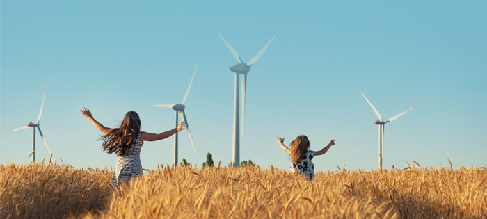 Two young people running happily through a field with turbines in the background