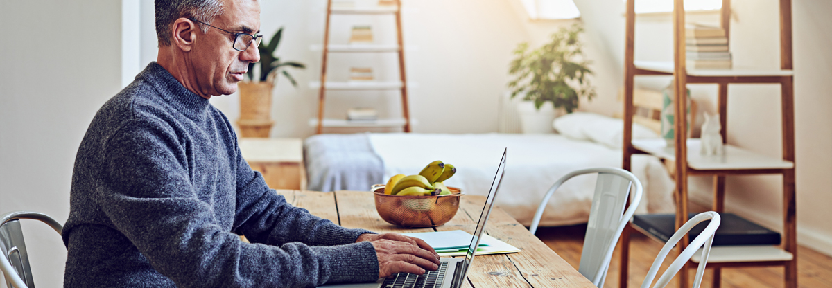 A man sitting at home typing on a laptop